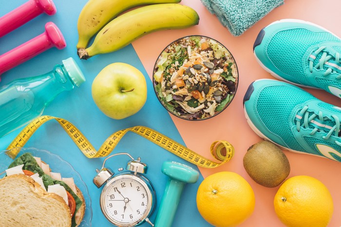 Fitness items with healthy food and alarm clock