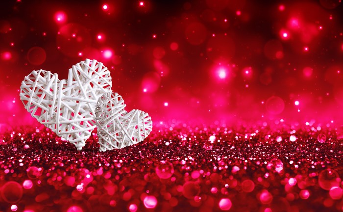 Two white wicker hearts on a red glitter background