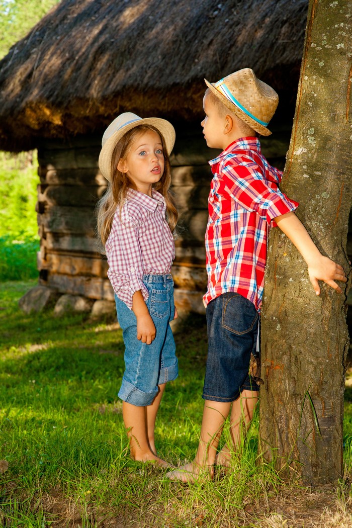 Two children in hats by a tree