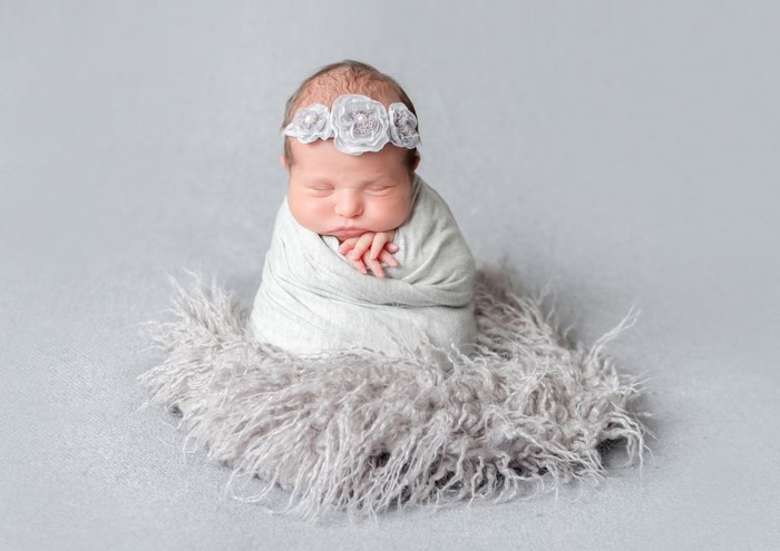 Newborn baby girl wrapped in a blanket with a floral headband