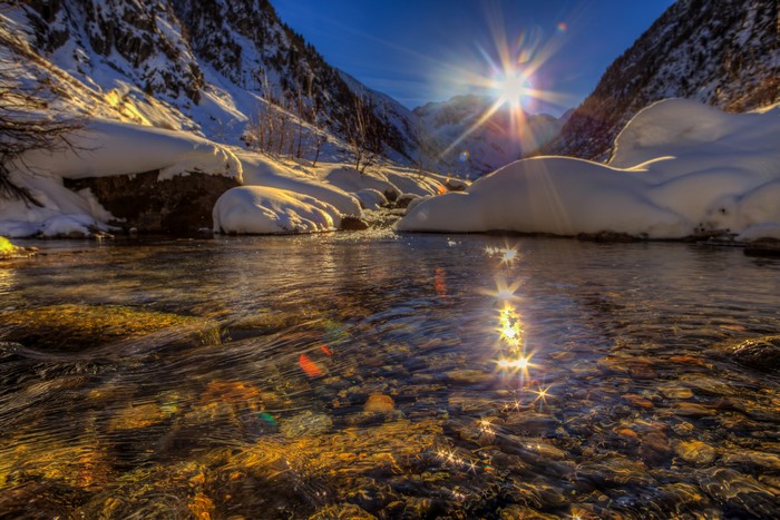 Sun shining over snowy mountains and a river in Goms, Switzerland