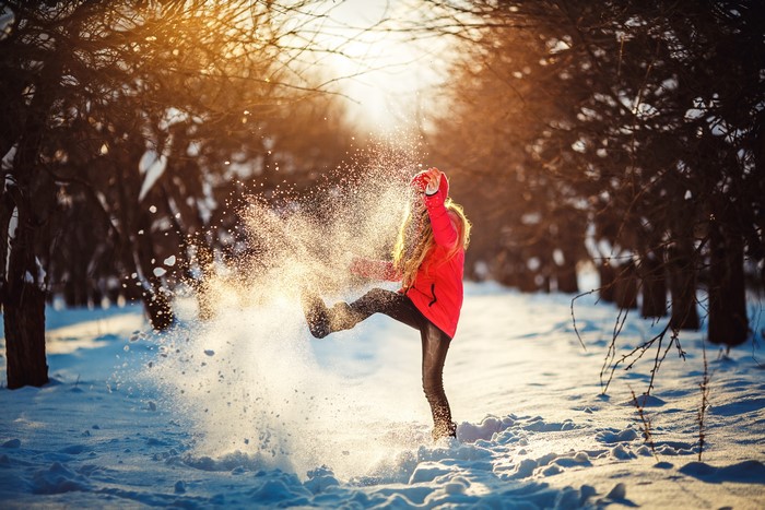 Girl kicking snow in winter forest