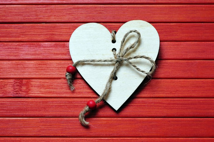 Wooden heart with twine and beads on red background