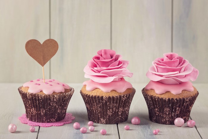 Three pink cupcakes with heart and rose decorations