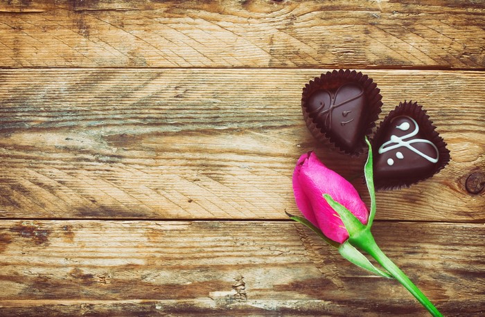 Heart-shaped chocolates and pink rose on wood