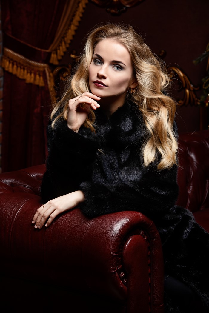 Blonde girl in fur coat sitting on a sofa