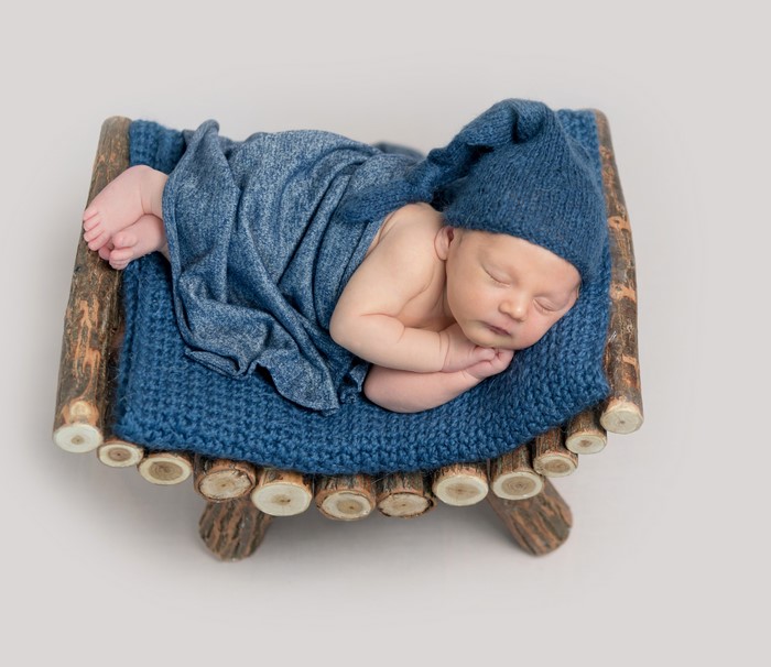 Newborn baby sleeping in a wooden cradle with a blue hat and blanket