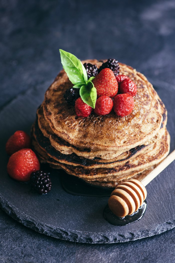 Stack of pancakes with berries and honey dipper