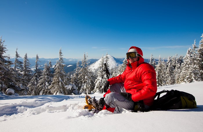 Man in red jacket with snowshoes in snowy mountains