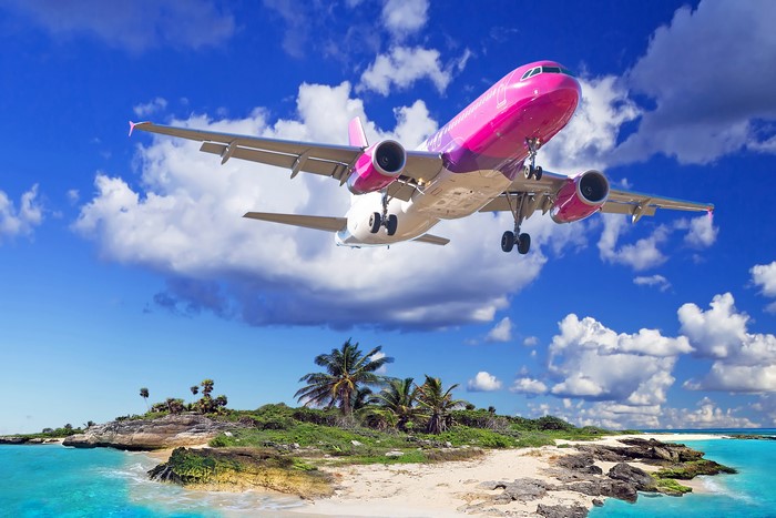 Pink airplane flying over a tropical island