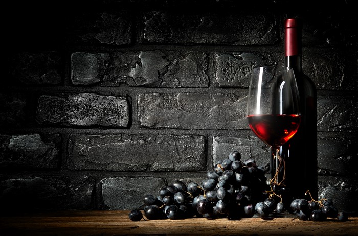Wine bottle, glass, and grapes against brick wall