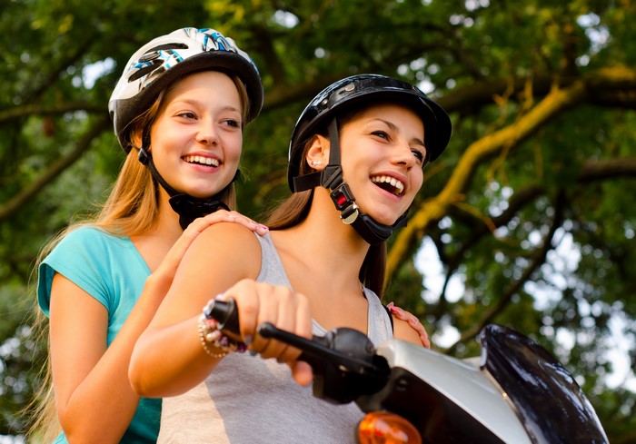 Two girls wearing helmets on a scooter