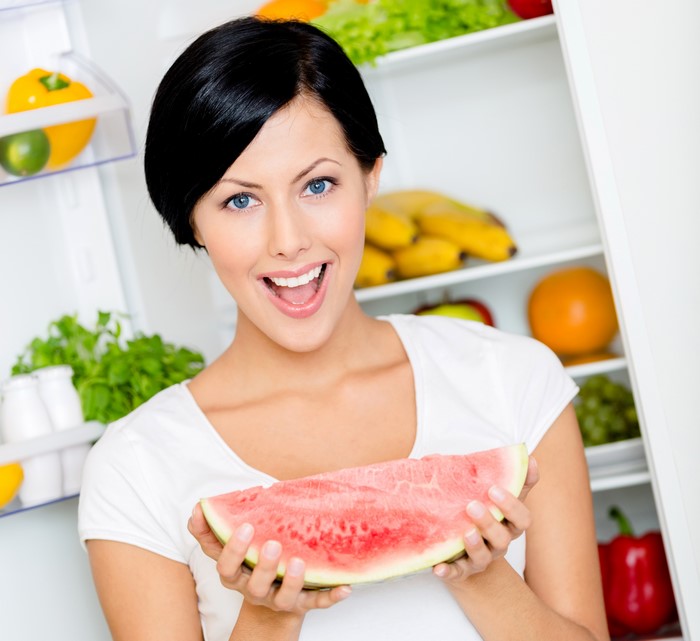 Brunette girl holding watermelon in refrigerator