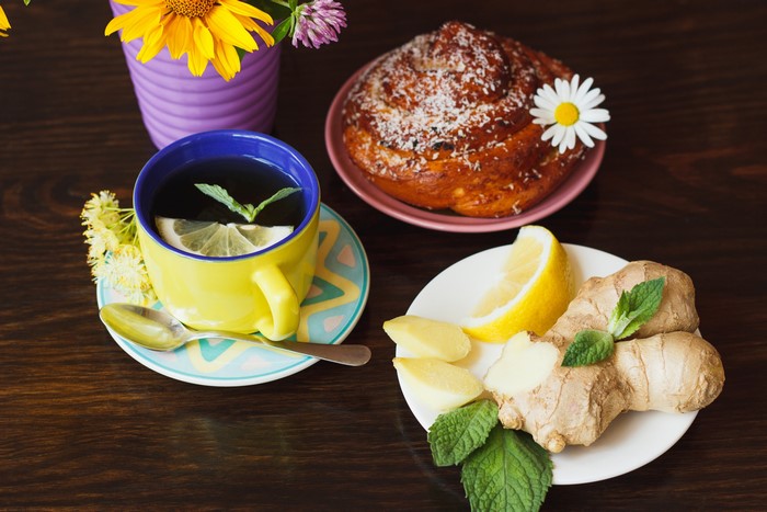 Tea with lemon, ginger, bun, and flowers