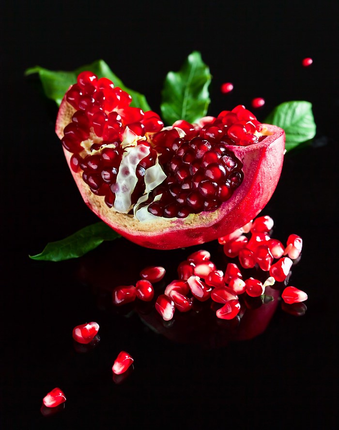 Pomegranate seeds and leaves on black background