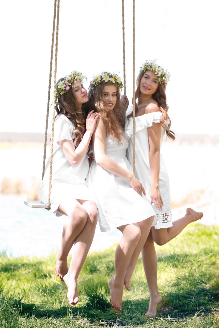 Three young women in white dresses on a swing