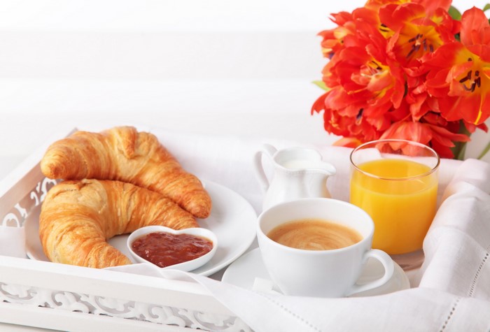 Breakfast tray with croissants, coffee, juice, and tulips
