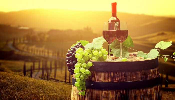 Wine bottle and glasses on barrel with grapes