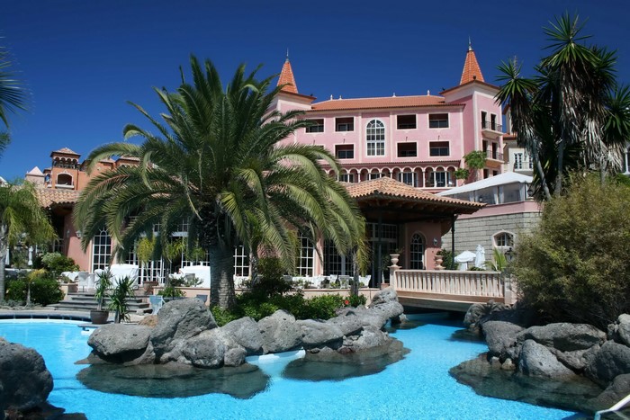 Pink resort building with palm trees and swimming pool in Tenerife