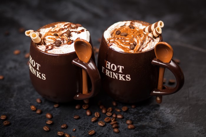 Two mugs of hot chocolate with whipped cream and coffee beans