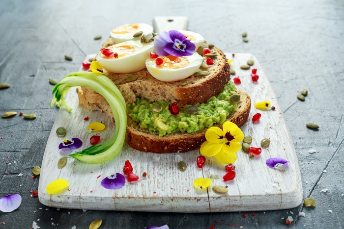 Avocado toast with eggs and edible flowers on a cutting board