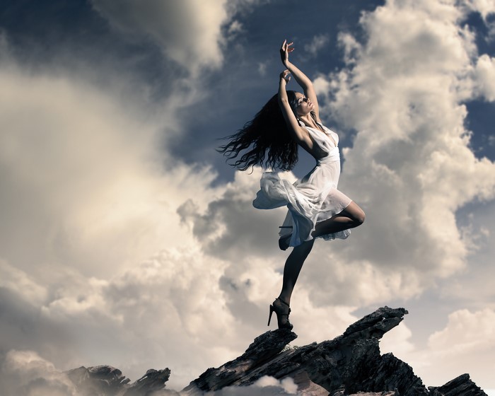 Woman in white dress dancing on rocks with clouds