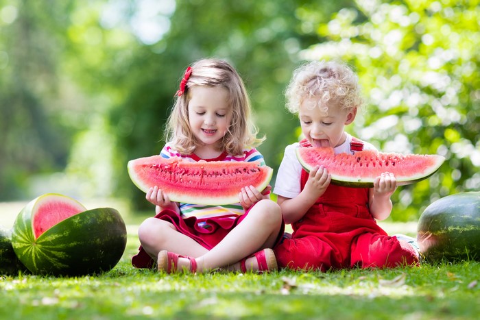 Two children eating watermelon in a park