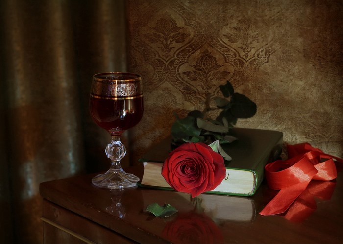 Still-life with red rose, wine glass, book, and ribbon