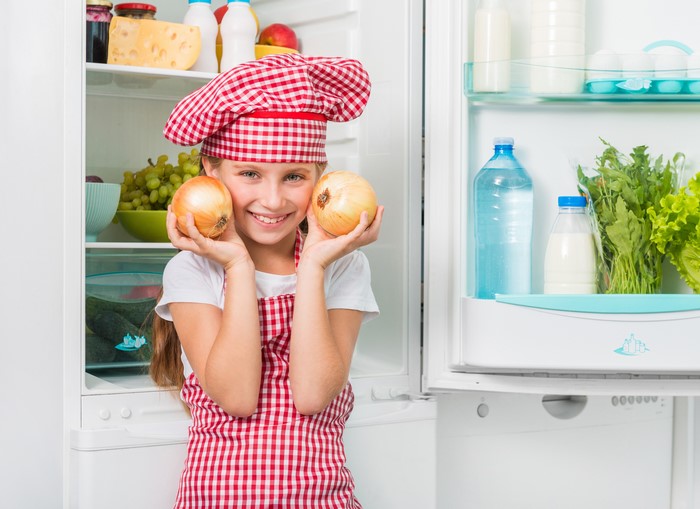 Girl in chef hat holding onions in front of refrigerator