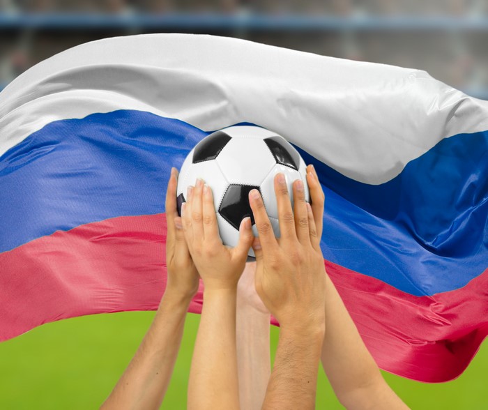 Hands holding a soccer ball in front of the Russian flag