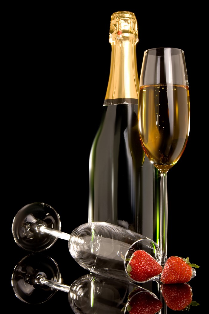 Champagne bottle, glass, and strawberries on black background