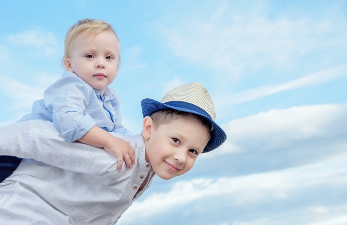 Two boys, one on the other's shoulders, against a blue sky