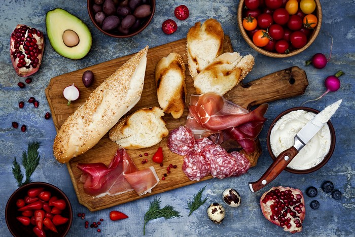 Charcuterie board with bread, meats, fruits, and vegetables