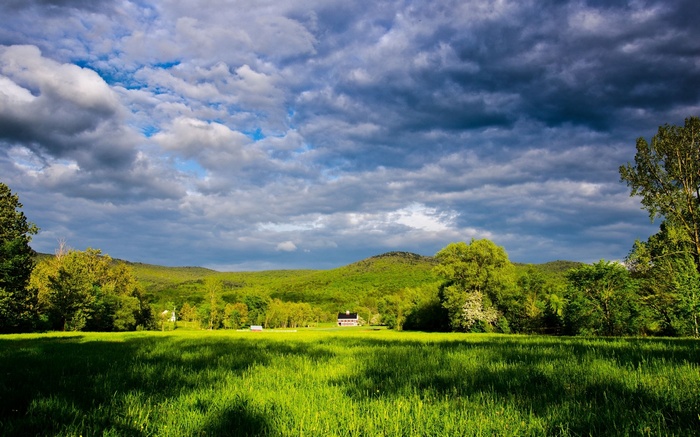 A house in a green valley under a cloudy sky