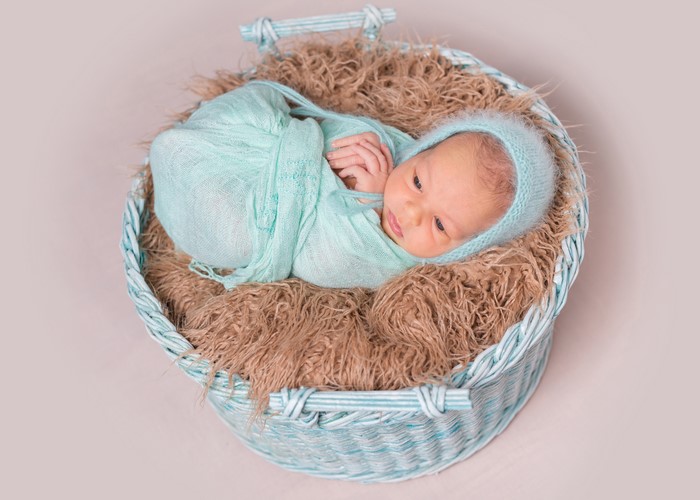 Newborn baby wrapped in a blue blanket in a wicker basket