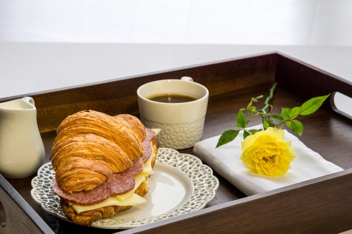 Breakfast tray with croissant sandwich, coffee, and yellow rose