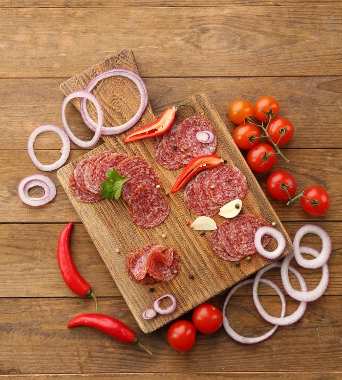 Sliced salami with tomatoes, onions, and peppers on cutting boards
