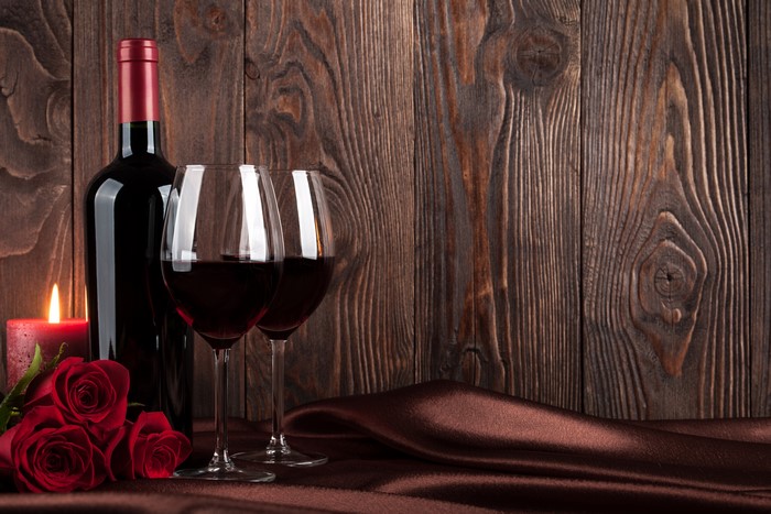 Wine bottle, glasses, roses, and candle on wood