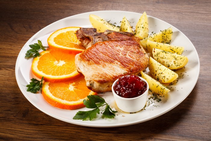 Pork chop with potatoes, orange slices, and cranberry sauce