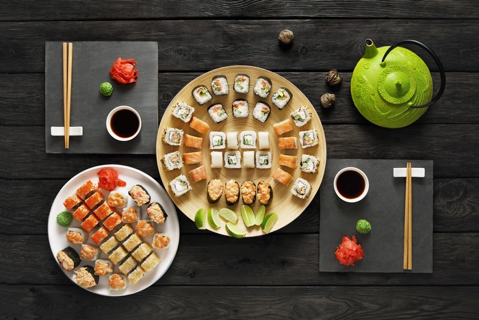 Sushi platter with teapot and chopsticks on dark wood