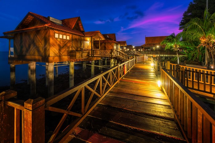 Wooden bungalows on stilts over water at dusk