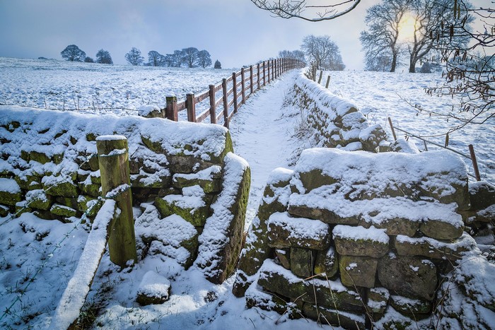 Snowy path with stone walls and wooden fence in Yorkshire, UK