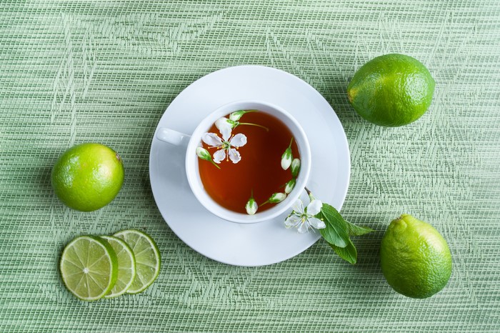 Tea with lime and flowers on a green background