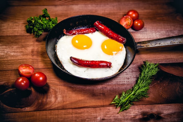 Fried eggs and sausages in a pan with tomatoes