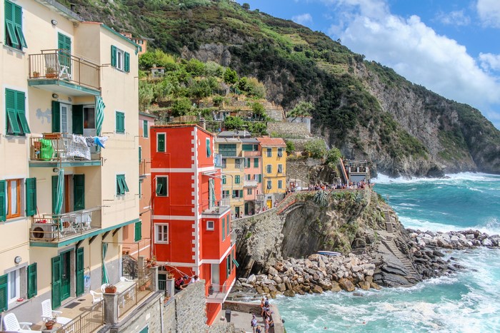 Colorful houses on a cliffside in Riomaggiore, Italy with waves crashing