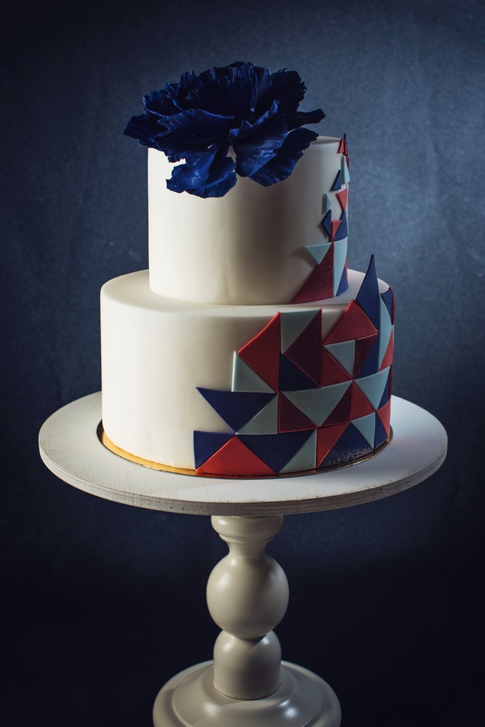 Two-tiered white cake with geometric design and blue flower