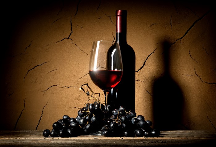 Wine bottle, glass, and grapes on a wooden surface