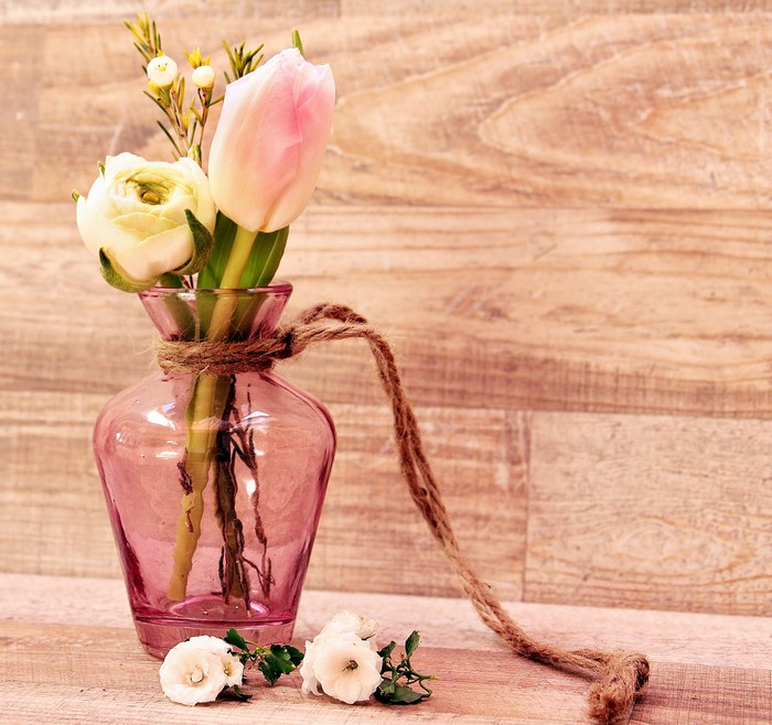 Pink vase with tulips and ranunculus on wood