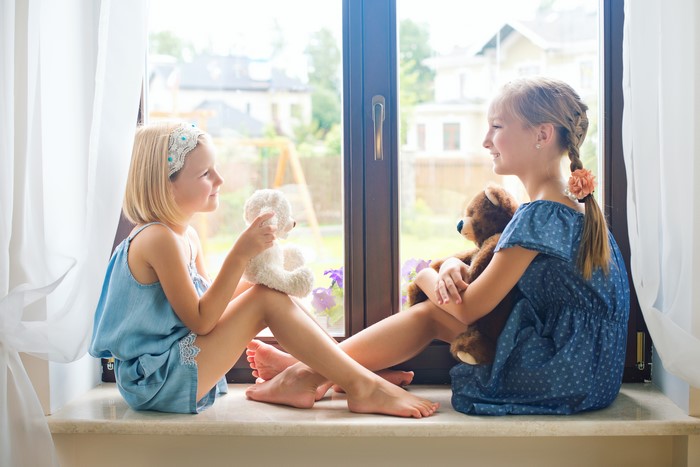 Two little girls with teddy bears by the window