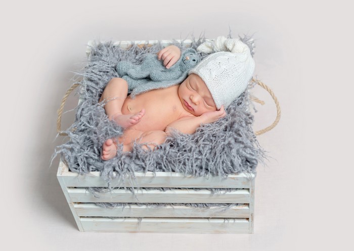 Newborn baby sleeping in a wooden crate with a toy